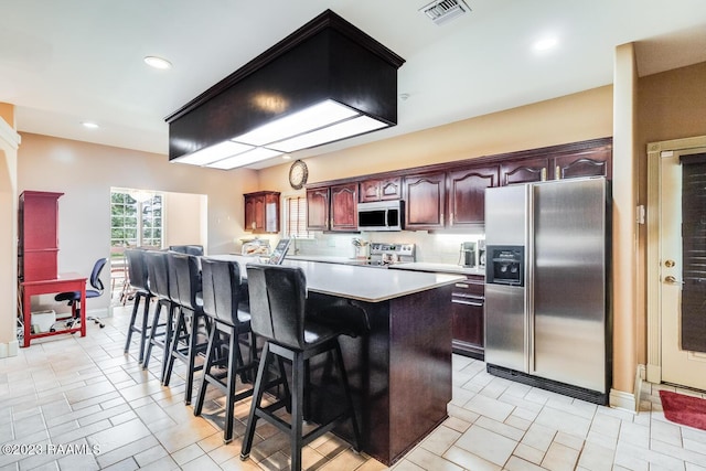 kitchen featuring visible vents, a kitchen island, a kitchen breakfast bar, stainless steel appliances, and light countertops