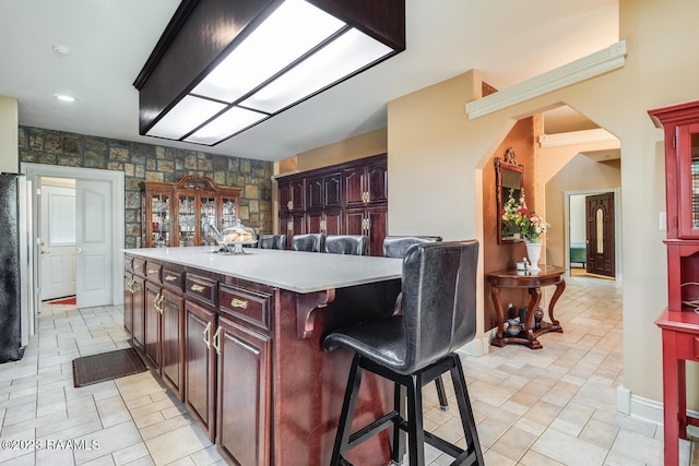 kitchen with arched walkways, a kitchen island, a breakfast bar area, freestanding refrigerator, and light countertops