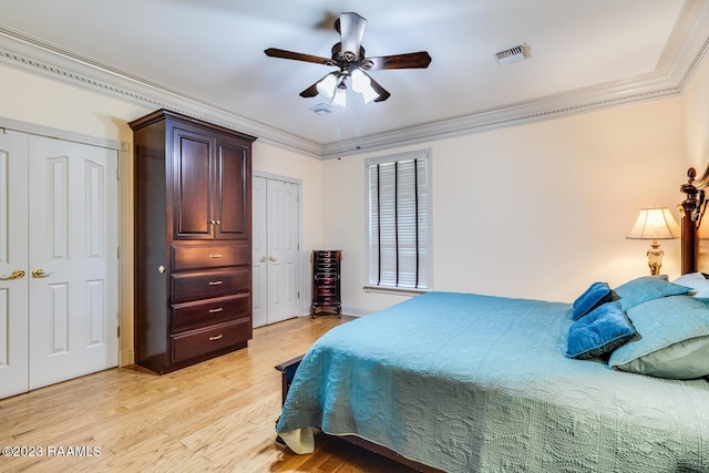 bedroom featuring light wood finished floors, visible vents, a ceiling fan, crown molding, and multiple closets