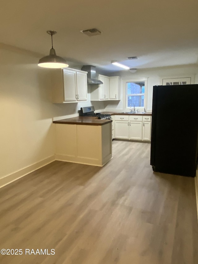 kitchen featuring visible vents, a peninsula, freestanding refrigerator, wall chimney exhaust hood, and a sink