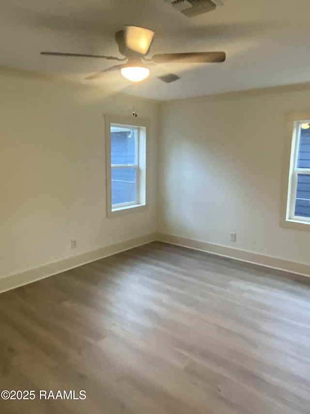 empty room featuring visible vents, a healthy amount of sunlight, baseboards, and wood finished floors