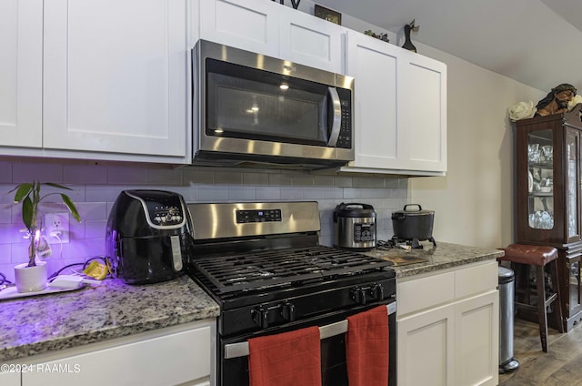 kitchen with white cabinets, wood finished floors, backsplash, and stainless steel appliances