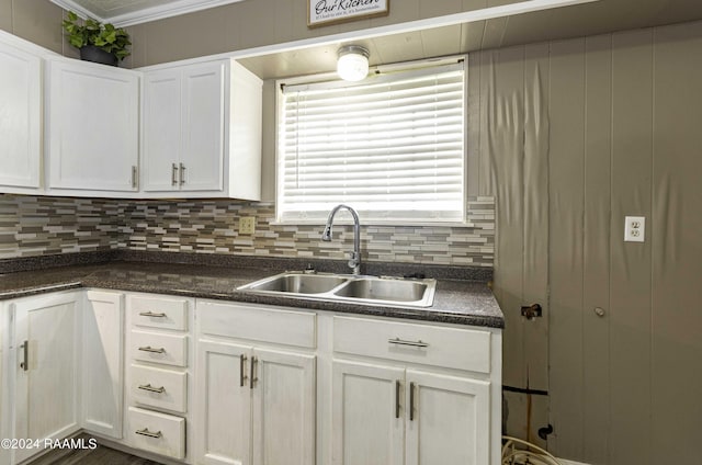 kitchen featuring dark countertops, decorative backsplash, white cabinetry, and a sink