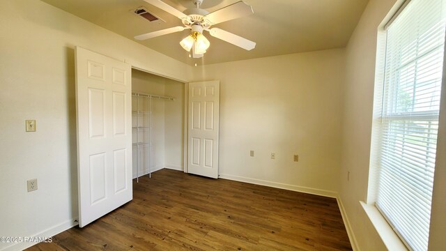 unfurnished bedroom with dark wood-style flooring, a closet, visible vents, ceiling fan, and baseboards