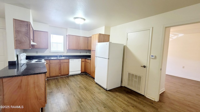 kitchen featuring dark countertops, visible vents, light wood-style flooring, a sink, and white appliances