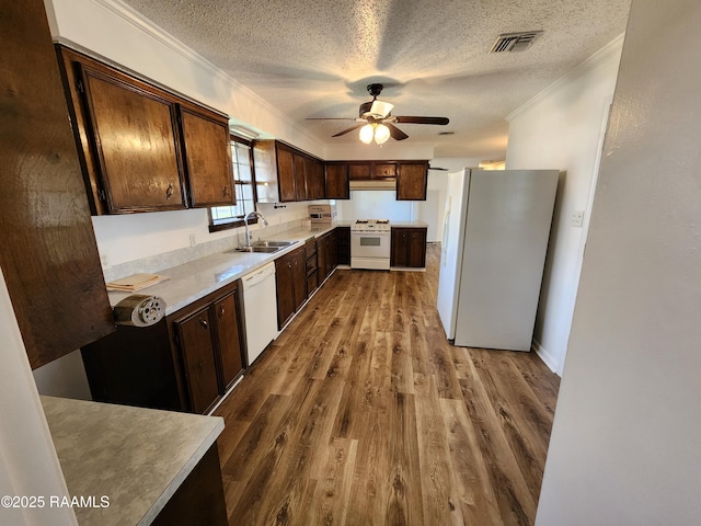 kitchen featuring crown molding, under cabinet range hood, dark wood-style floors, white appliances, and a sink