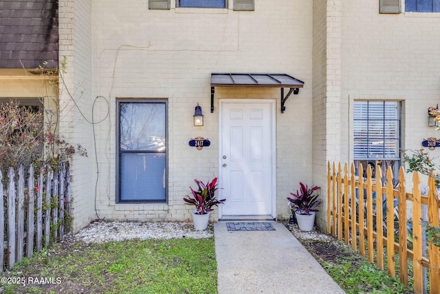 doorway to property featuring brick siding and fence