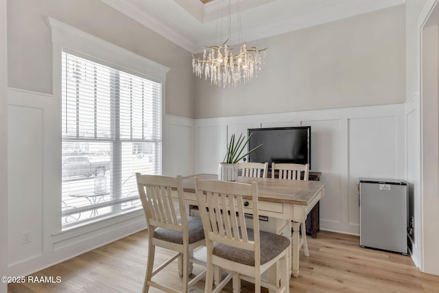 dining area with a wainscoted wall, light wood finished floors, crown molding, a decorative wall, and a notable chandelier