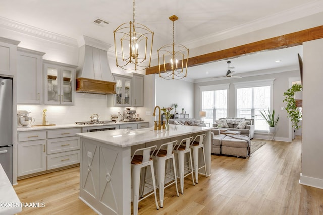 kitchen featuring custom exhaust hood, a center island with sink, appliances with stainless steel finishes, and light wood-style flooring