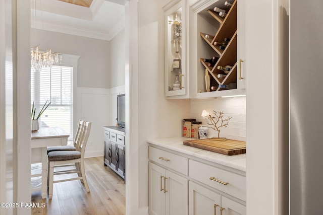 bar with light wood finished floors, backsplash, wainscoting, a decorative wall, and crown molding