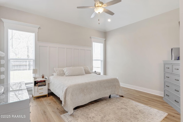 bedroom with multiple windows, a ceiling fan, light wood finished floors, and wainscoting