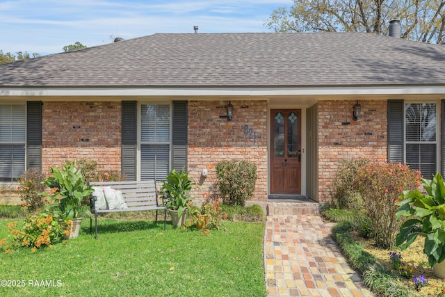 doorway to property with brick siding, a shingled roof, and a yard