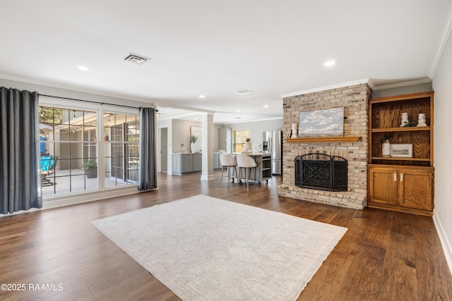 living area with crown molding, a brick fireplace, dark wood-style floors, and visible vents