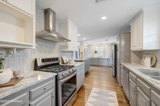 kitchen featuring light wood-style flooring, gray cabinets, light stone counters, stainless steel appliances, and wall chimney range hood