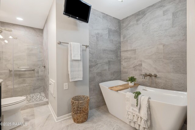 full bath with baseboards, a freestanding bath, toilet, a stall shower, and tile walls