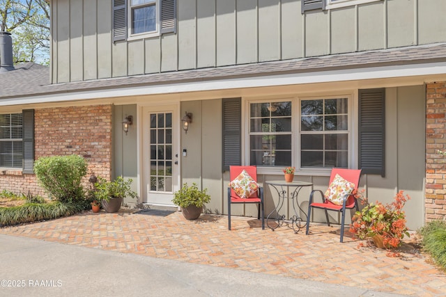 property entrance with brick siding, board and batten siding, covered porch, and a shingled roof