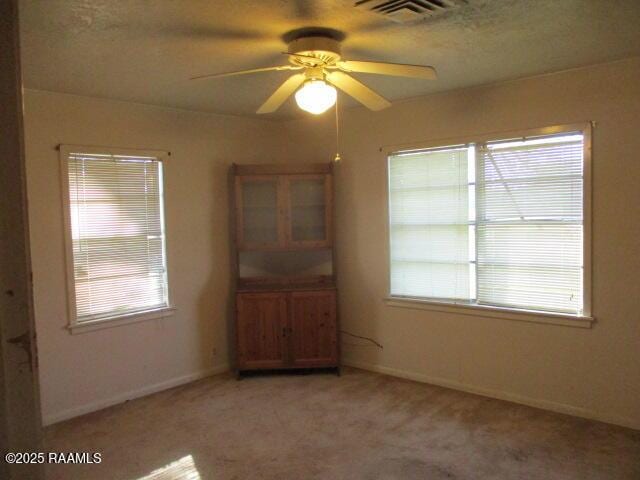 empty room with visible vents, light carpet, baseboards, and ceiling fan