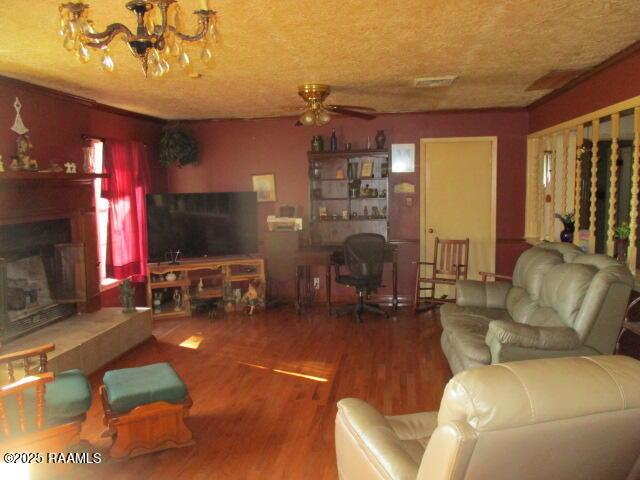 living area featuring wood finished floors, visible vents, a fireplace with raised hearth, a textured ceiling, and ceiling fan with notable chandelier