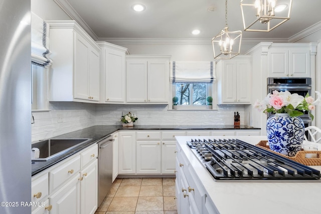 kitchen with ornamental molding, backsplash, stainless steel appliances, white cabinets, and a chandelier