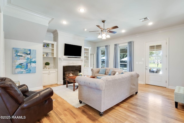 living room with visible vents, a fireplace, ornamental molding, ceiling fan, and light wood-type flooring