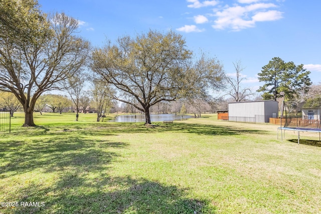 view of yard featuring a water view, a trampoline, an outbuilding, and fence