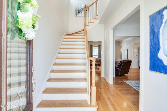 stairs with crown molding and wood finished floors