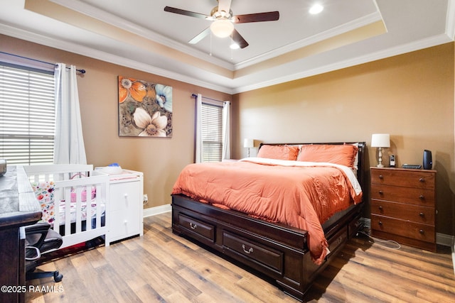 bedroom with a tray ceiling, baseboards, light wood-style flooring, and crown molding