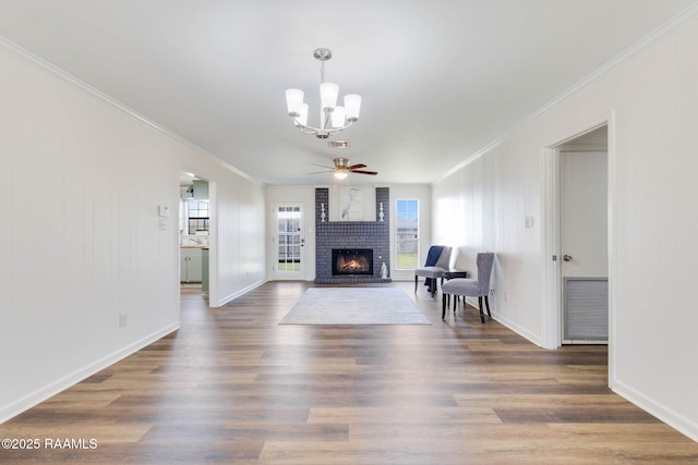 unfurnished living room with ceiling fan with notable chandelier, wood finished floors, a fireplace, and crown molding