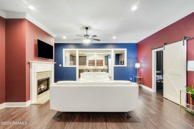 living area with a barn door, wood finished floors, baseboards, and ornamental molding