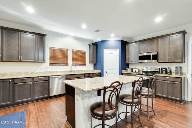 kitchen featuring stainless steel appliances, a kitchen bar, visible vents, and wood finished floors