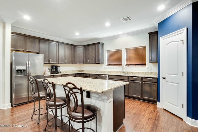 kitchen with visible vents, ornamental molding, dark brown cabinetry, appliances with stainless steel finishes, and a kitchen breakfast bar