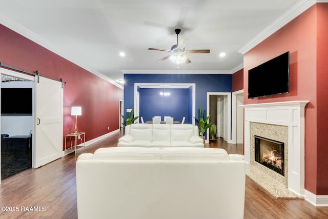 living area with a barn door, a ceiling fan, wood finished floors, and crown molding