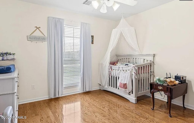 bedroom with baseboards, a crib, wood finished floors, and a ceiling fan