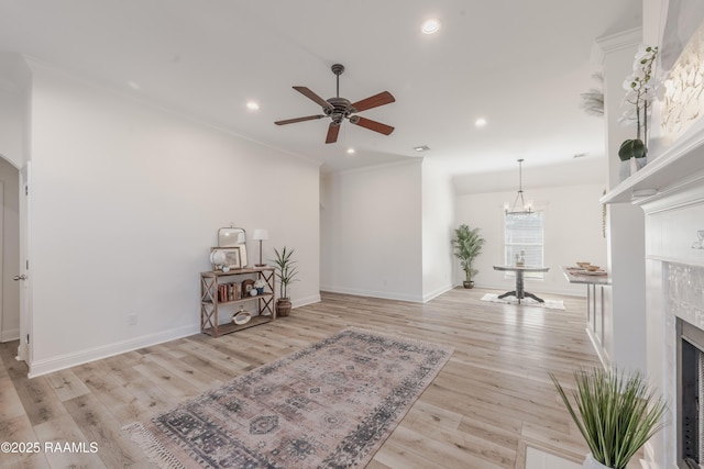 living area featuring baseboards, a fireplace, light wood-style floors, crown molding, and ceiling fan with notable chandelier