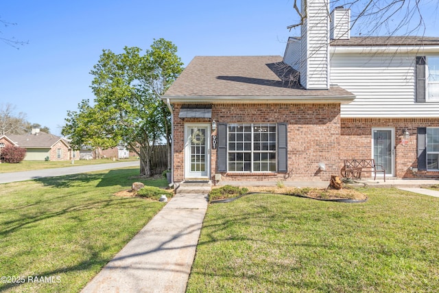 view of front facade with a front yard, brick siding, a chimney, and a shingled roof