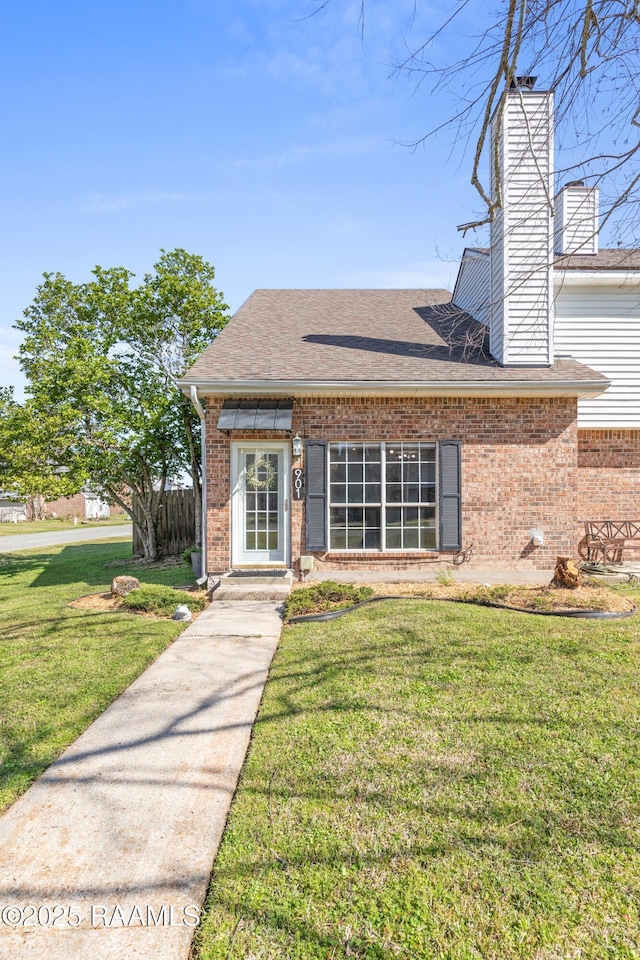 view of front of property with brick siding, a chimney, a front lawn, and a shingled roof