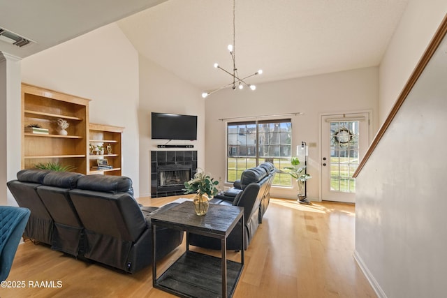 living area featuring high vaulted ceiling, light wood-style floors, visible vents, and a tile fireplace