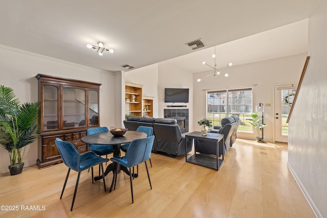 dining space featuring light wood-style flooring, a fireplace, visible vents, and a chandelier