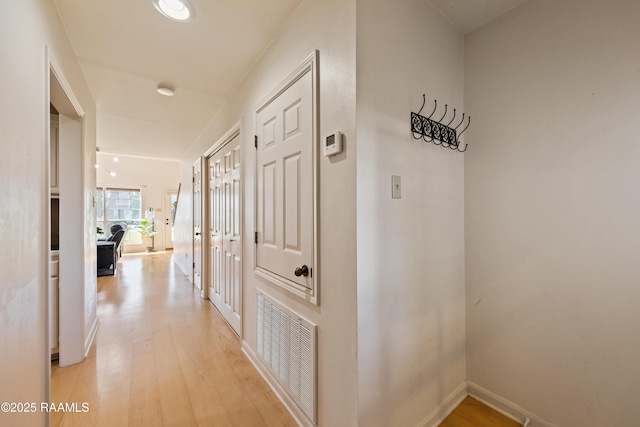 corridor with light wood-type flooring, visible vents, and baseboards