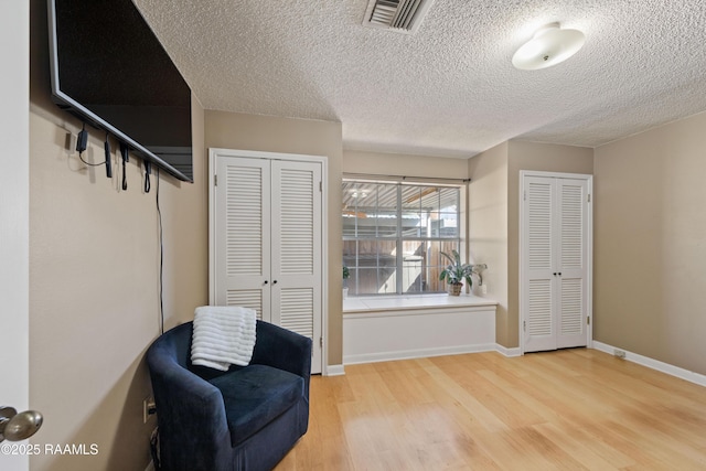 living area featuring light wood-type flooring, visible vents, baseboards, and a textured ceiling