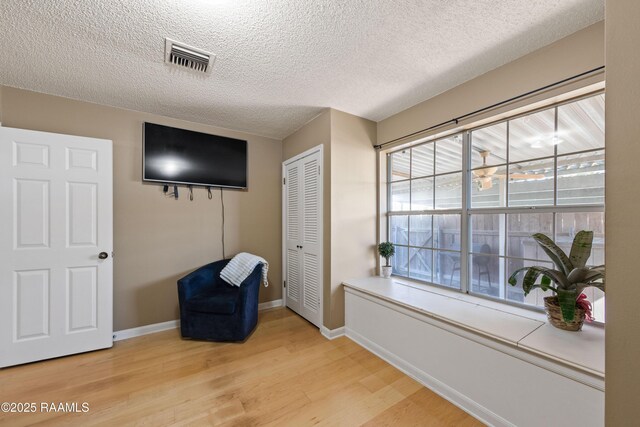 sitting room with light wood finished floors, visible vents, a textured ceiling, and baseboards