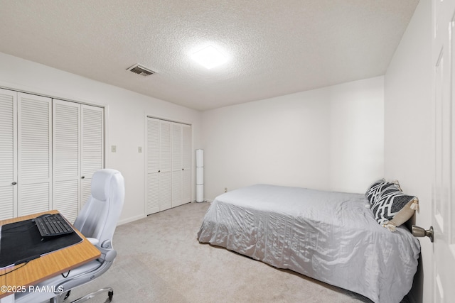 carpeted bedroom with baseboards, visible vents, two closets, and a textured ceiling