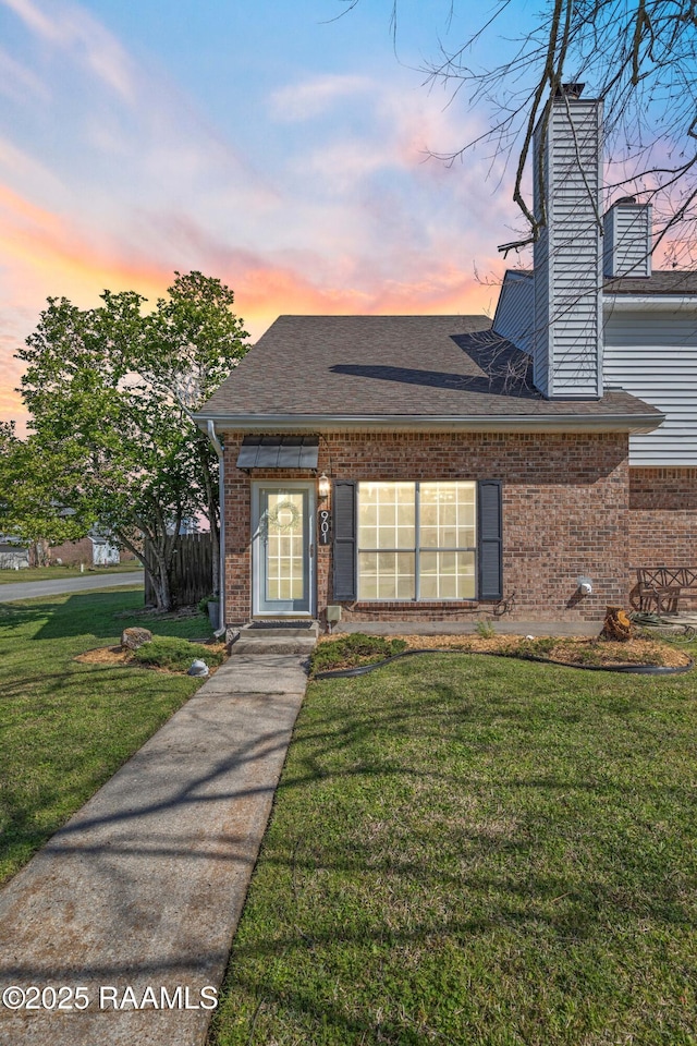 view of front facade featuring a front yard, a chimney, brick siding, and a shingled roof