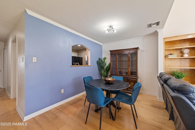 dining space featuring visible vents, light wood-type flooring, baseboards, and ornamental molding