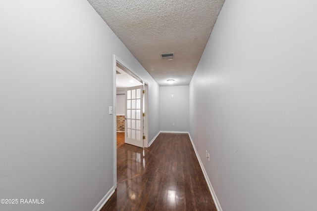 corridor featuring visible vents, dark wood-type flooring, a textured ceiling, and baseboards