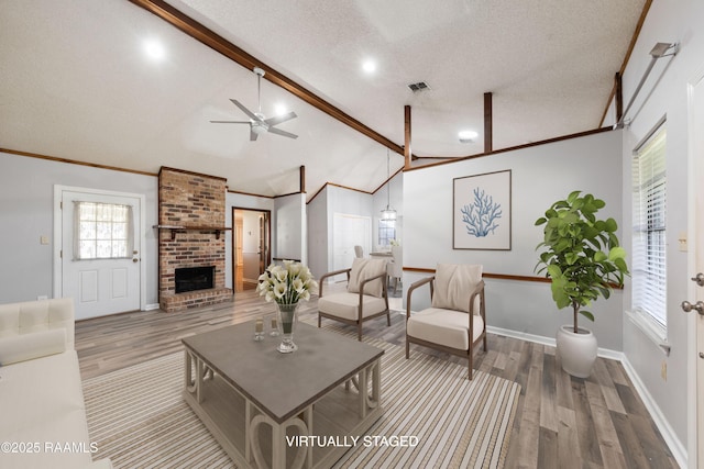 living area with a fireplace, vaulted ceiling with beams, a textured ceiling, and wood finished floors