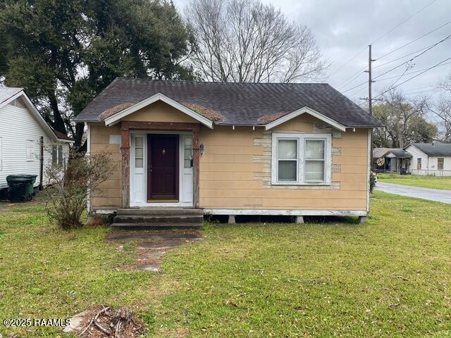 bungalow-style home with a shingled roof, a front yard, and entry steps