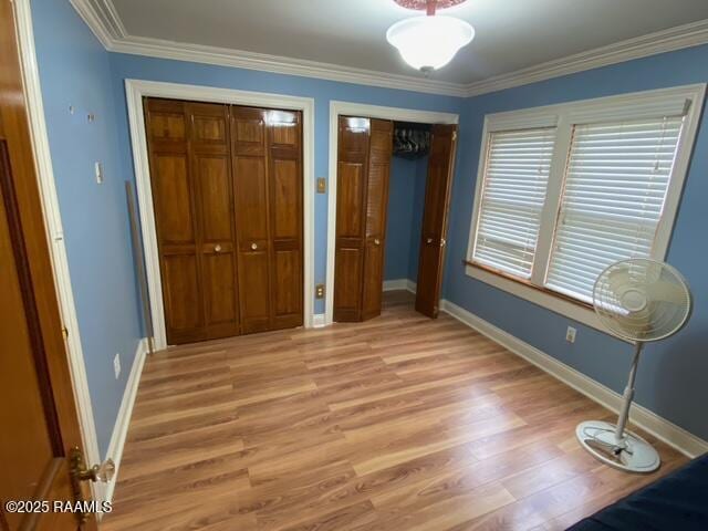 unfurnished bedroom with baseboards, multiple closets, light wood finished floors, and ornamental molding