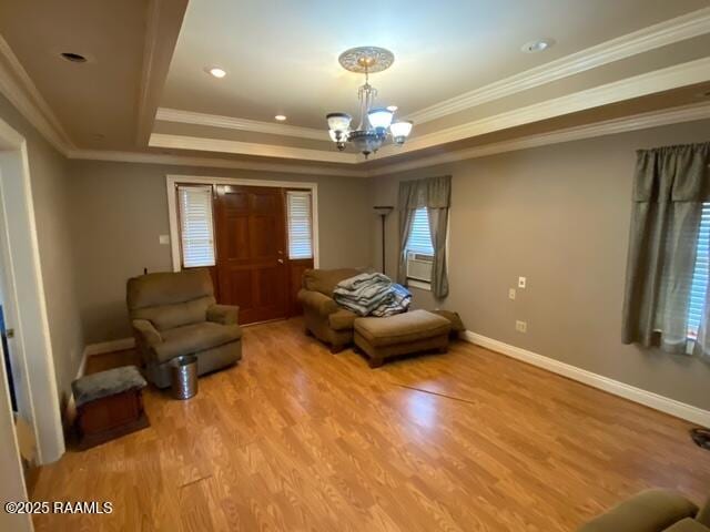 living room featuring wood finished floors, baseboards, a tray ceiling, crown molding, and a notable chandelier