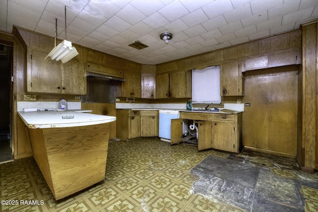 kitchen featuring brown cabinets, wooden walls, white dishwasher, and light countertops